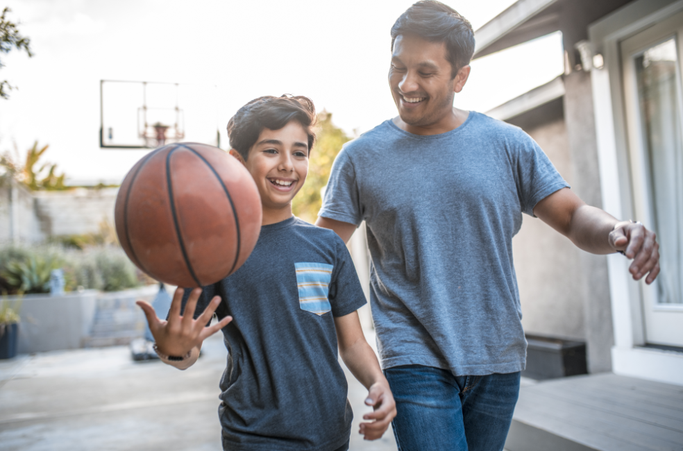 Happy boy spinning basketball while walking by father.